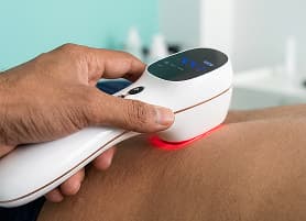 Handheld laser therapy device emitting red light on patient's skin