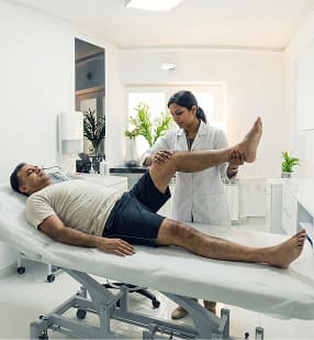 Clean physical therapy room with treatment bed, desk and teal chairs