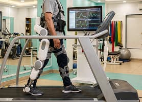 Person wearing robotic exoskeleton walking on treadmill in physiotherapy clinic
