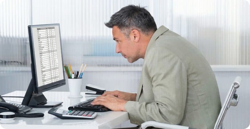 Office worker leaning toward his monitor with a hunched, forward head posture at his desk