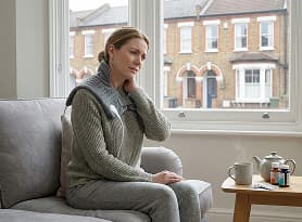 Woman on sofa with neck pain during a virtual physiotherapy session at home