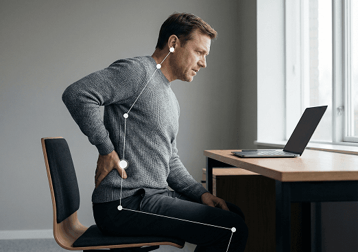 Man holding his lower back in pain while standing at a desk