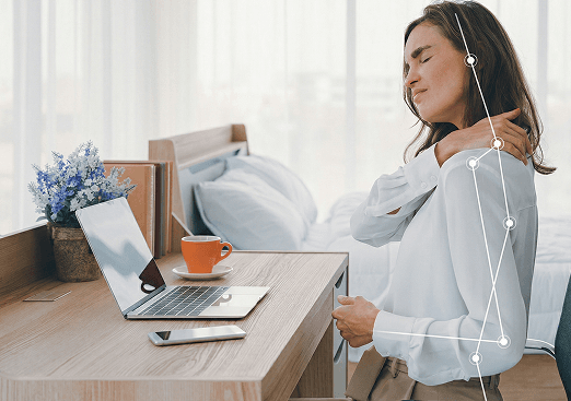 Woman sitting at a desk holding her shoulder in pain